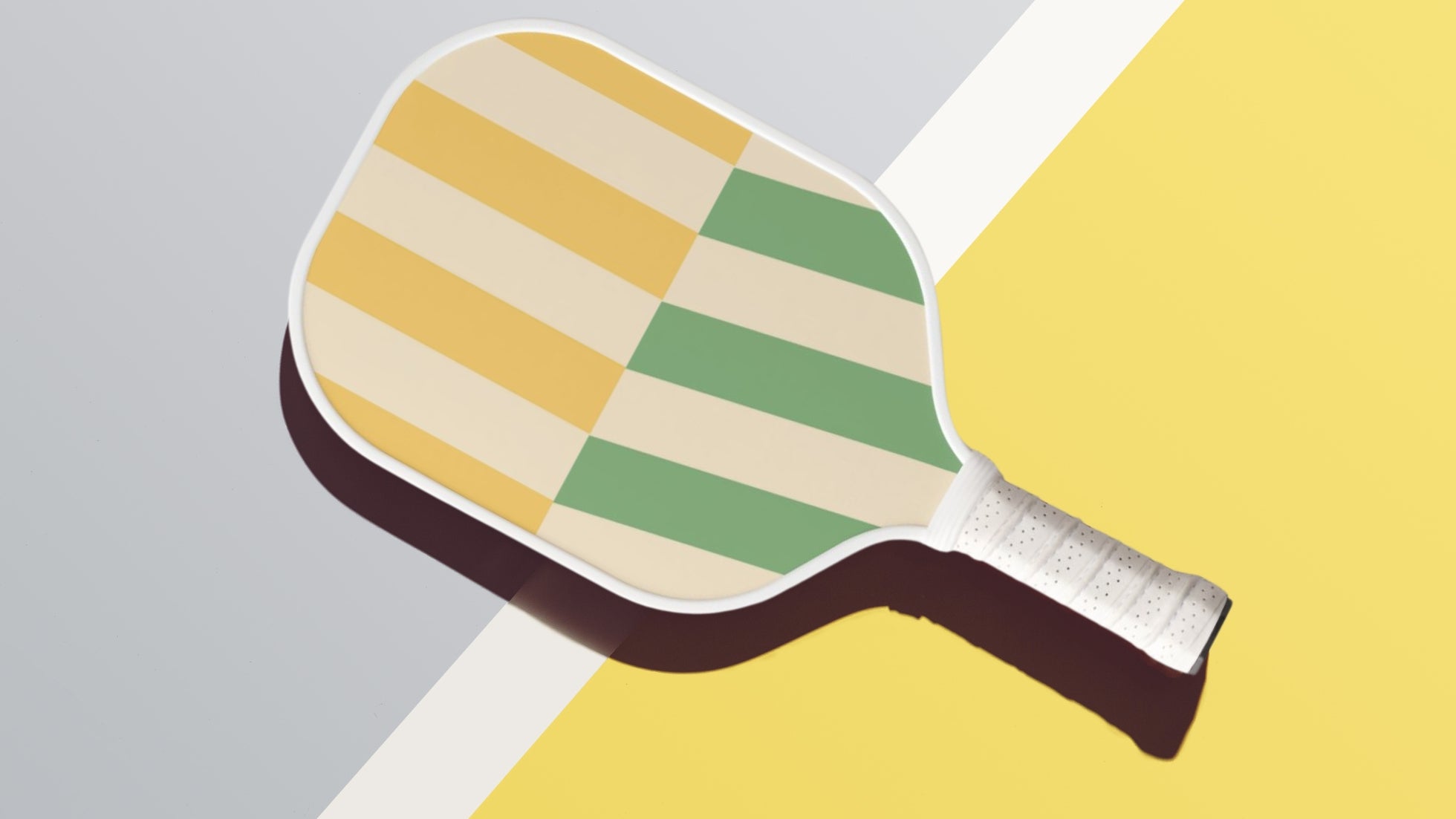 Image of a pickleball paddle with retro-style diagonal stripes in yellow, green, and cream colors, set against a background featuring contrasting diagonal sections in grey and yellow